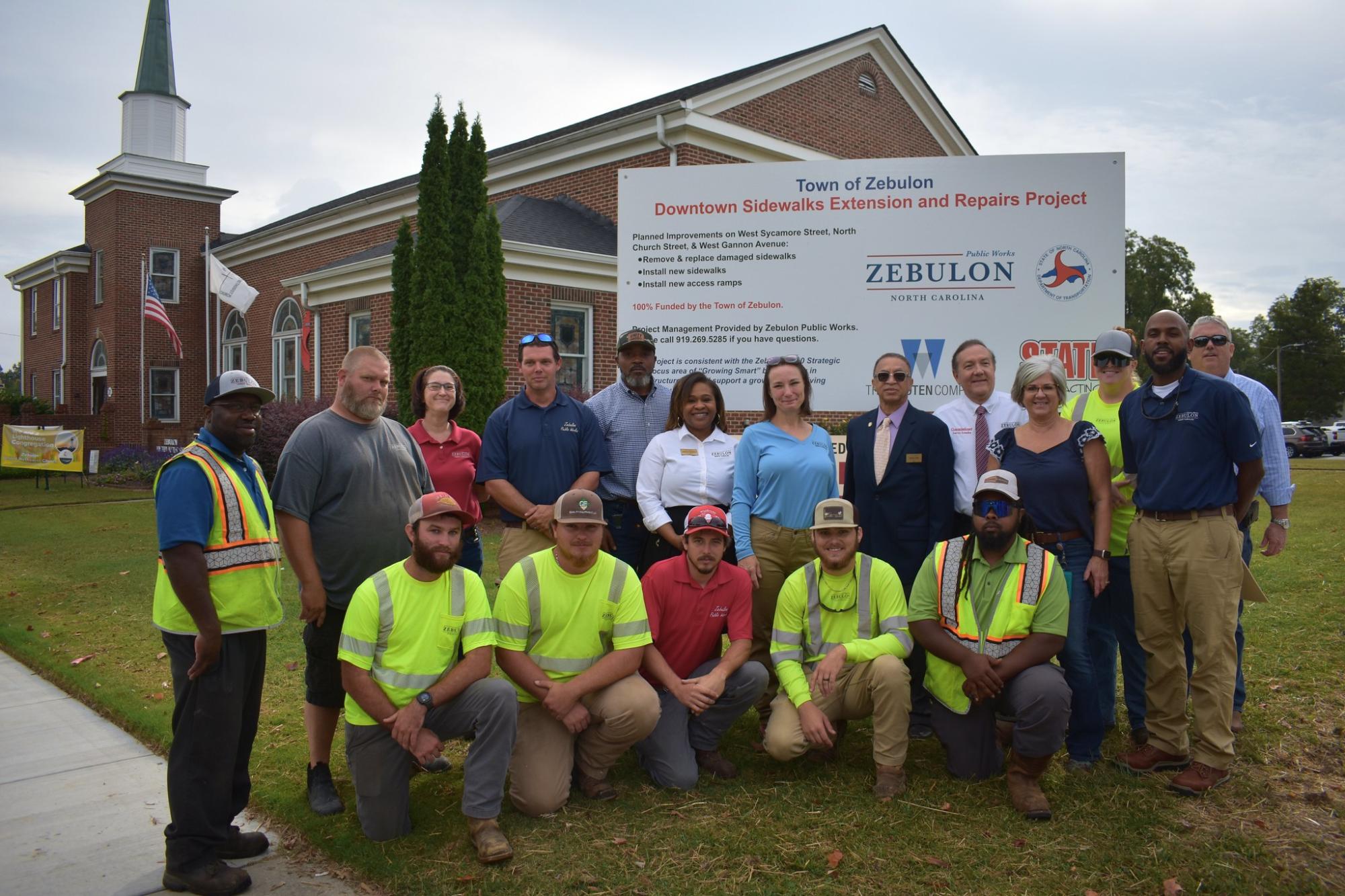 Public Works Posing in Front of the Sidewalk Project Sign